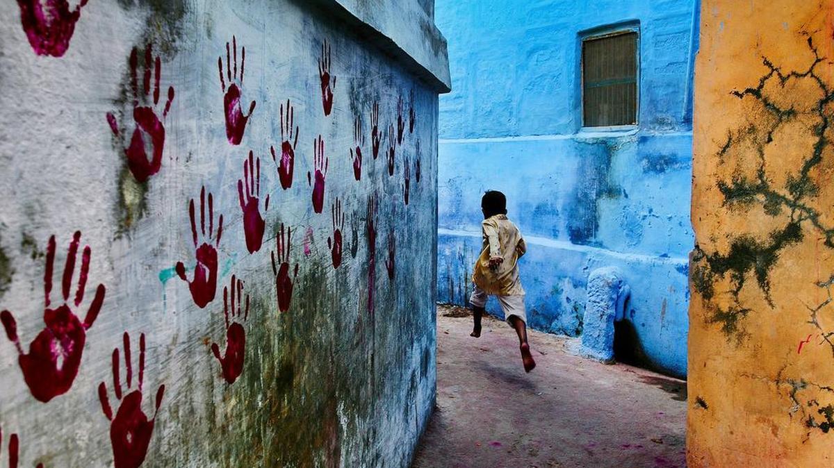 A young boy dashes through the narrow alleyways of Jodhpur, Rajasthan, in Steve McCurry’s “Boy in Mid-Flight.”