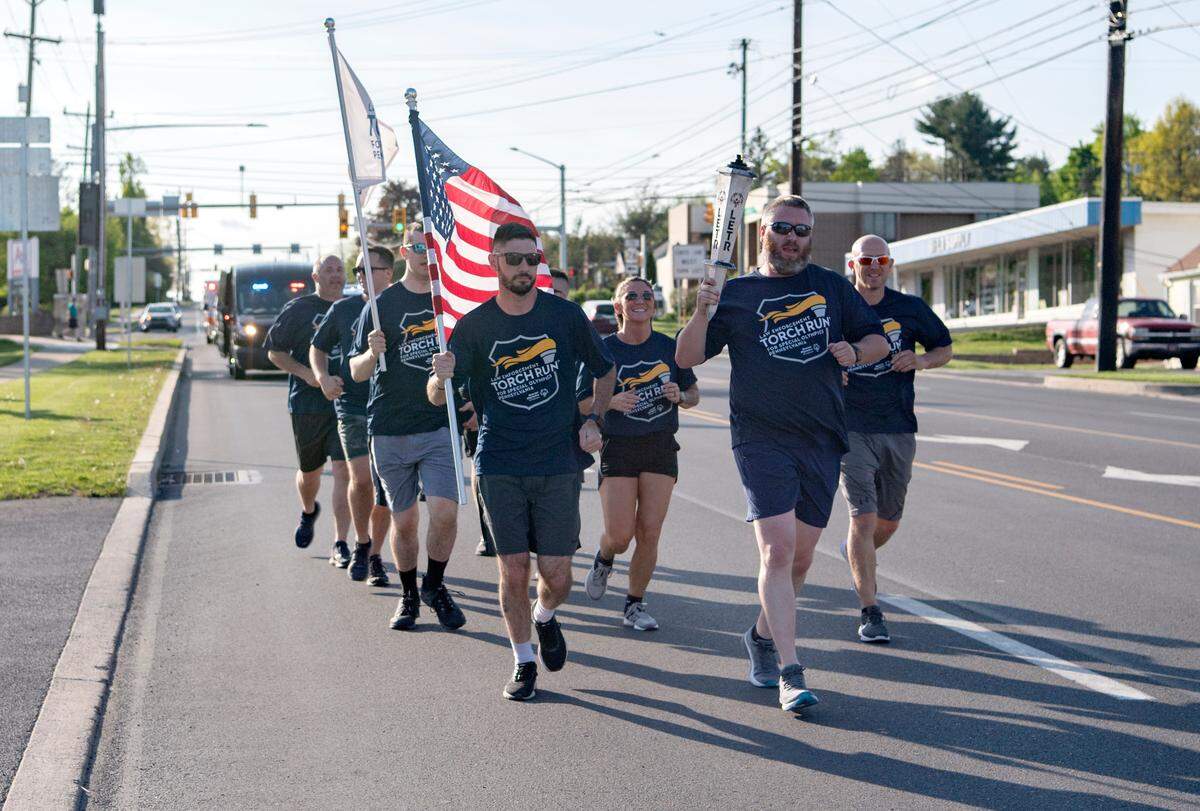 Members of the Ferguson Township police department run the final leg of the Law Enforcement Torch Run for the Special Olympics on Thursday, May 12, 2022. Carrying the American Flag is Bryan Greene and Derek Hoover carries the torch as they run along North Atherton Street.