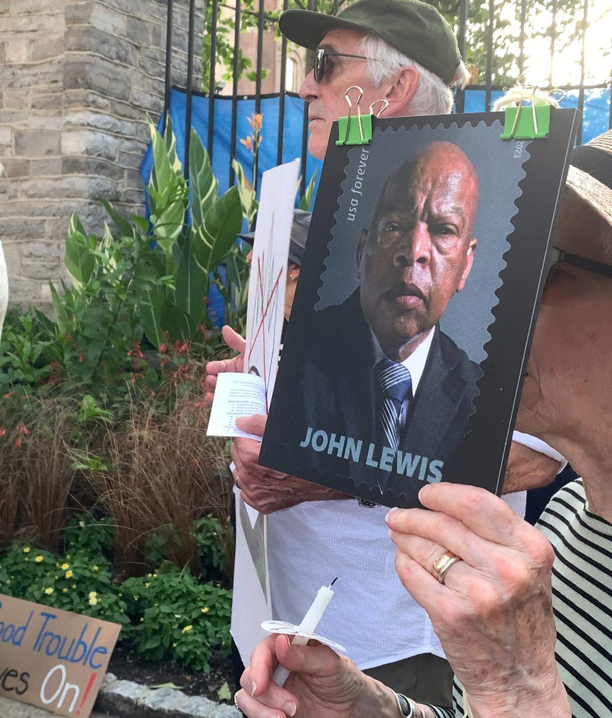 As protesters lit candles and sang “We Shall Overcome,” a protester held up a sign of the late John Lewis on Thursday, July 17, 2025.