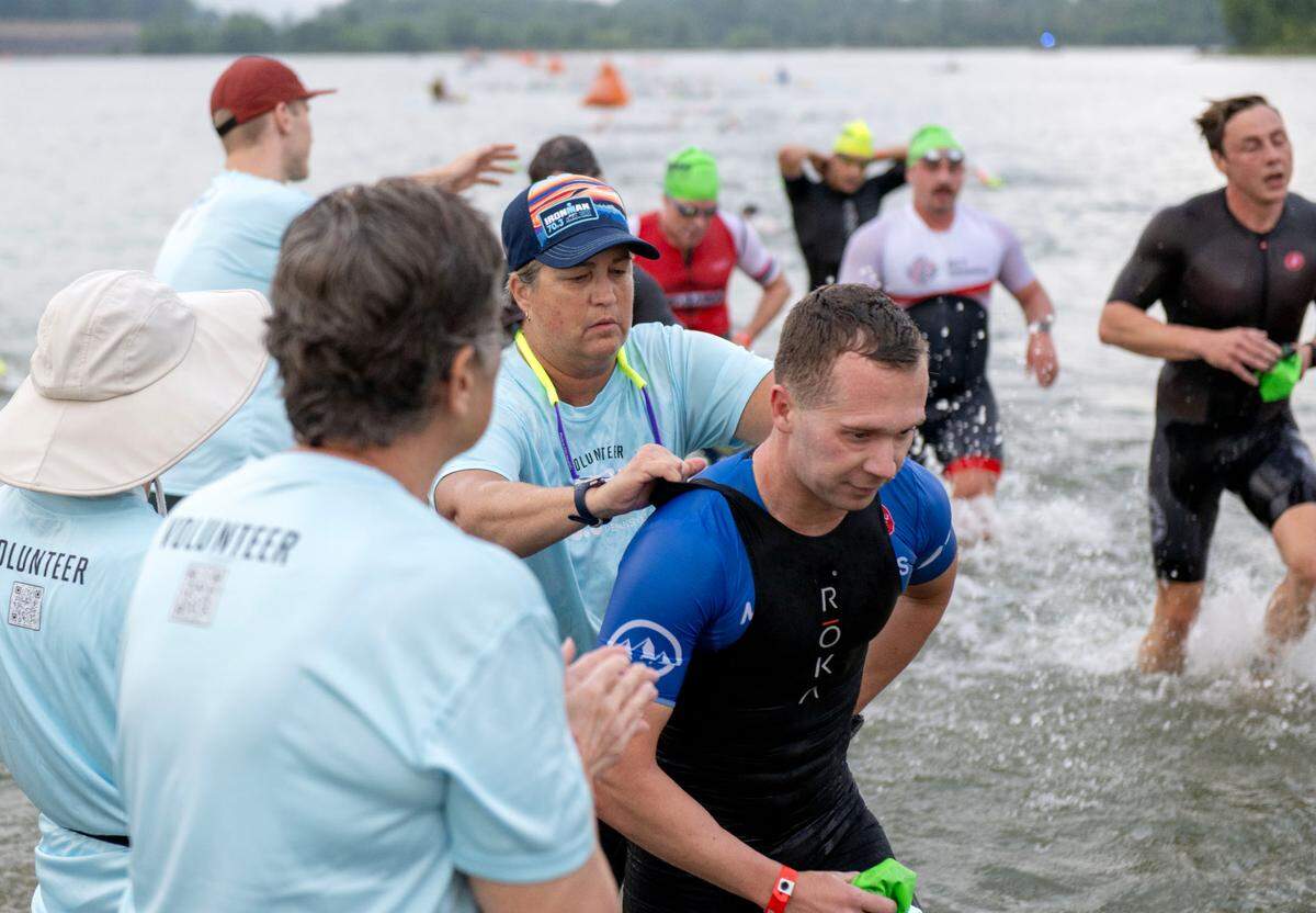 A volunteer unzips a swimmer as they run out of the water from the 1.2 mile swim in the Ironman 70.3 Pennsylvania Happy Valley on Sunday, June 30, 2024.