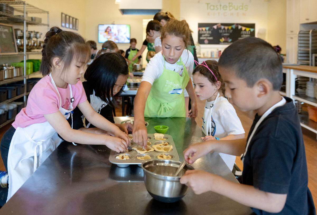 Counselor in training Taylor helps a table of campers make deep dish pizza cups during Taste Buds Kitchen summer camp on Tuesday, July 1, 2025.
