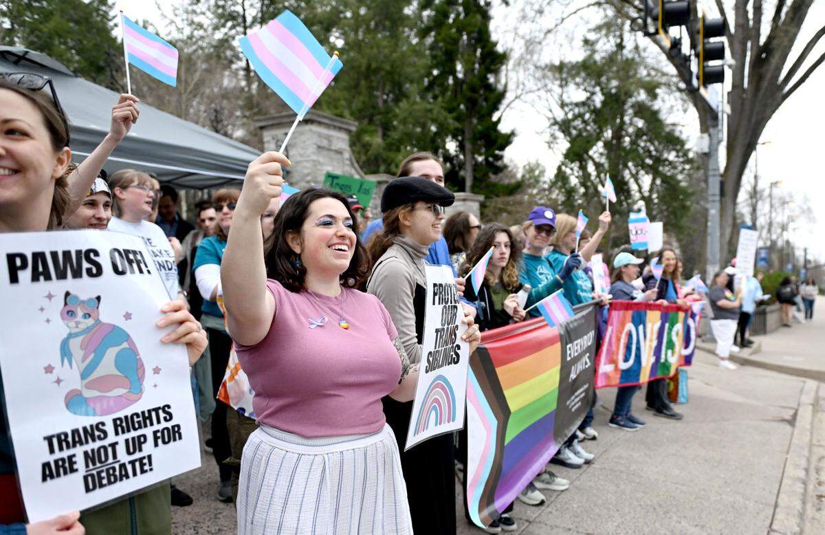 Sophia Mills waves a transgender flag during the Centre LGBT+’s Transgender Day of Visibility celebration at the Allen Street gates on Monday, March 31, 2025.