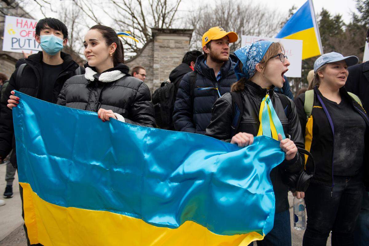Nelia Mihai (left) and Hannah Scholze (right) hold a Ukrainian flag during a protest against the Russian invasion of Ukraine in front of the Allen Street Gates on Thursday, Feb. 24, 2022 in State College, Pa.