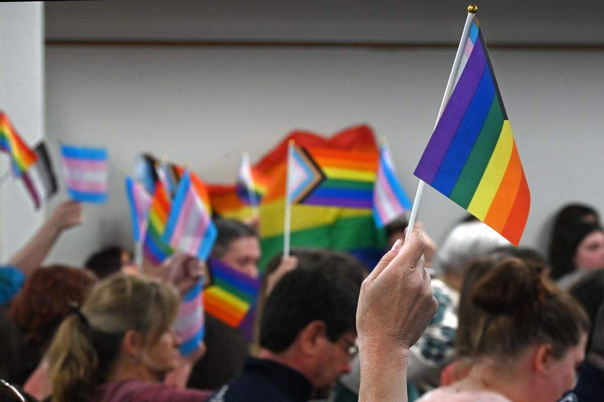 Audience members wave Pride flags while a parent speaks during the public comment period of the Central Bucks School District meeting in May 2022.