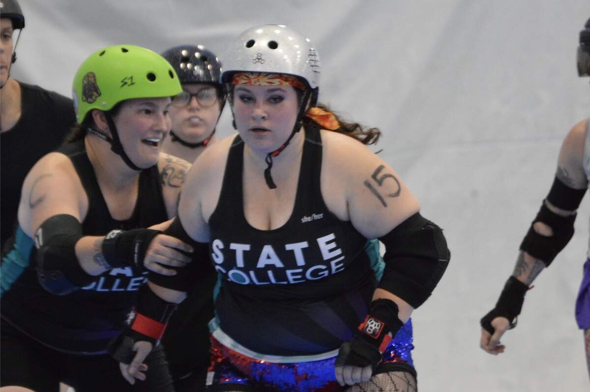 Two roller derby players skate in colorful helmets and protective gear during a game.