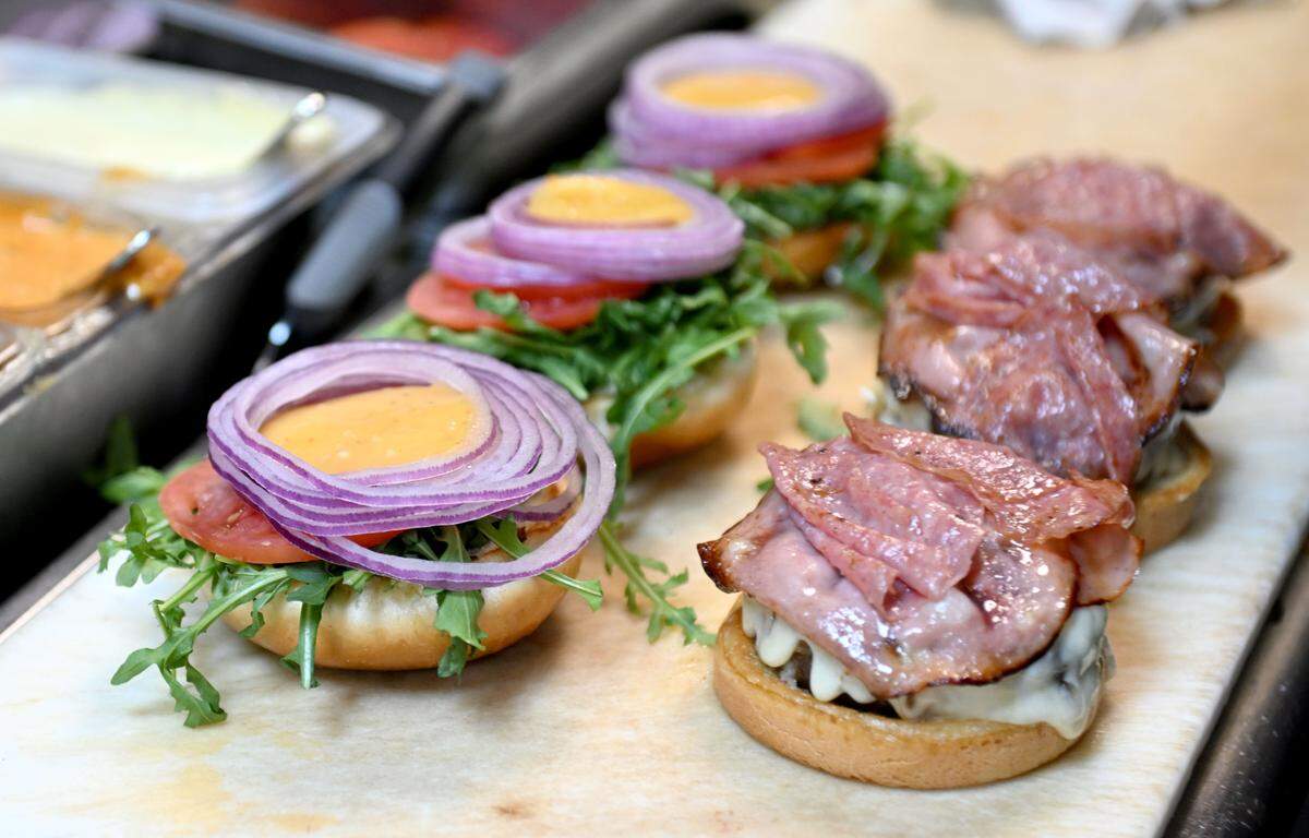 Several Coach Campbell’s Roman Burgers are prepared at The Field. The burger features salami, mortadella, white cheddar, arugula, tomato, onion, mayo and Italian dressing on a brioche bun.