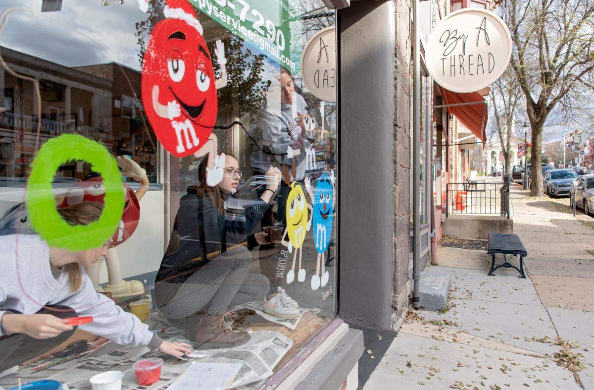 A trio of Bellefonte High School art students paint a festive scene on the window of M & M Copy Service on High Street on Tuesday, Nov. 23, 2021. Students painted windows throughout town.