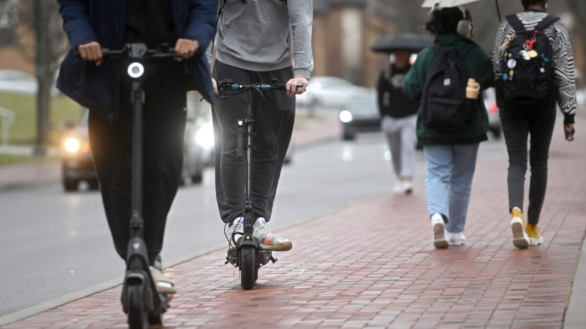 Two people ride scooters as others walk along Pollock Road on Penn State’s University Park campus Friday, March 31, 2023.