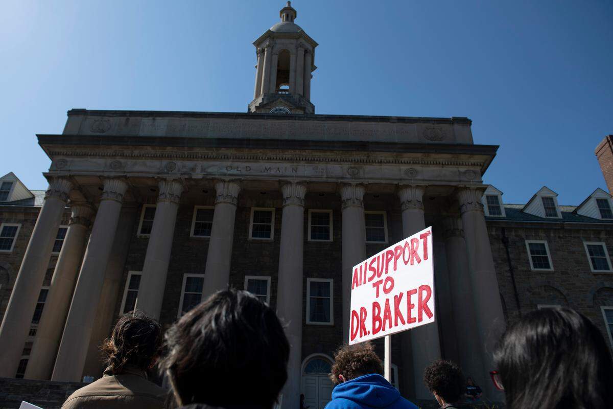 A protester holds a sign in front of Penn State’s Old Main Thursday during a rally to to protest termination proceedings for professor Oliver Baker.