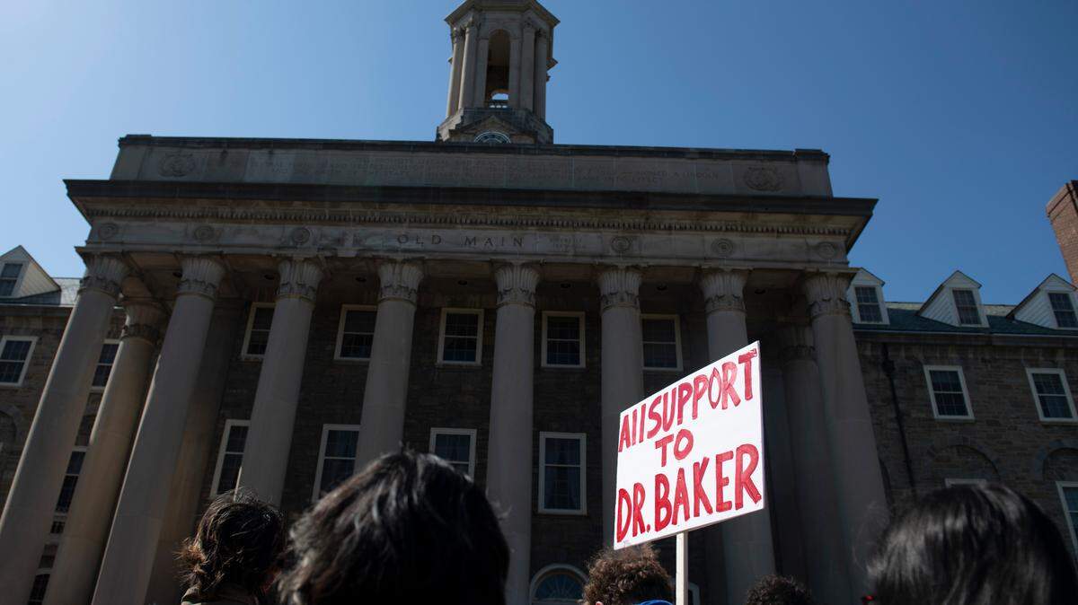 A protester holds a sign in front of Penn State’s Old Main during a rally to protest termination proceedings against Professor Oliver Baker in University Park, Pa., Thursday, April. 28, 2022.