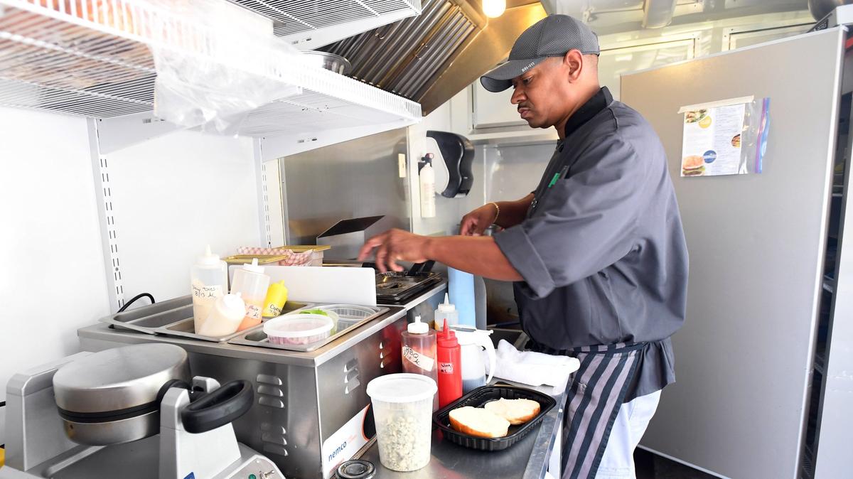 Happy Dishes owner Michael Johnson prepares “The Happy Burger” in August in his State College food trailer.