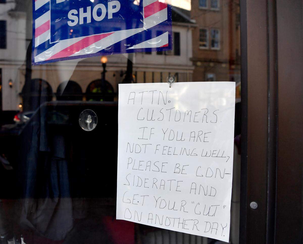A sign hanging in the window of Rinaldo’s Barber Shop on Friday encourages customers to not come in if they aren’t feeling well.