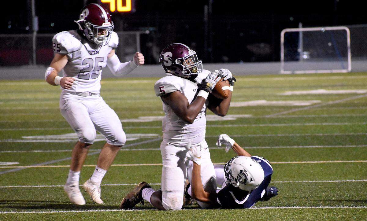 State College’s Isaiah Edwards (5) wrestles an interception away from Chambersburg receiver Kevin Lee (1), as linebacker Ryan Domico celebrates in the background. The interception helped to fuel the Little Lions’ second-half surge in a 27-17 road win. Edwards followed his pick with receiving and rushing touchdowns.