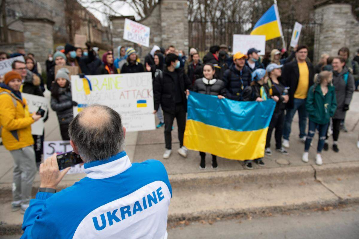A man in a Ukraine track jacket takes a photo during a protest against the Russian invasion of Ukraine in front of the Allen Street Gates on Thursday.