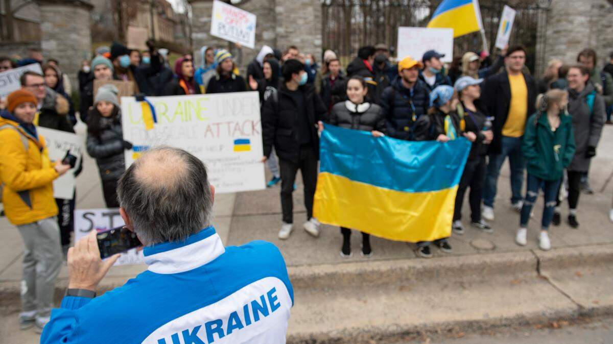 A man in a Ukraine track jacket takes a photo during a protest against the Russian invasion of Ukraine in front of the Allen Street Gates on Thursday, Feb. 24, 2022 in State College, Pa.