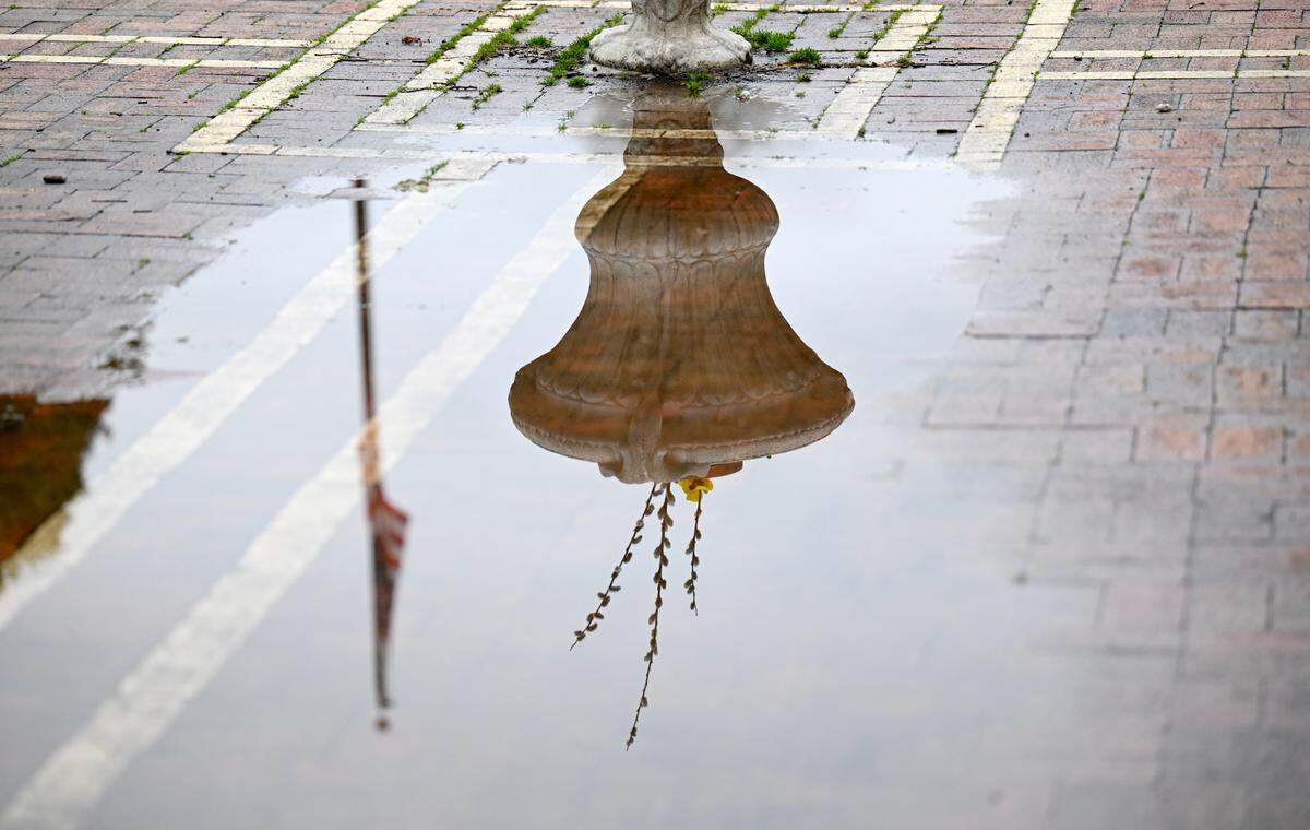 The American Flag and a flower pot reflected in a large puddle In Talleyrand Park on April 11, 2025.