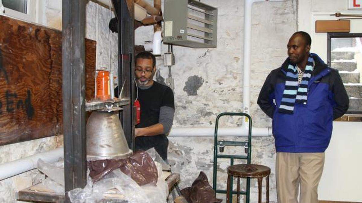 Stephen Carpenter II demonstrates how to use his original filter press to make a ceramic water filter while Nigerian potter Ibukunoluwa Ayoola looks on.
