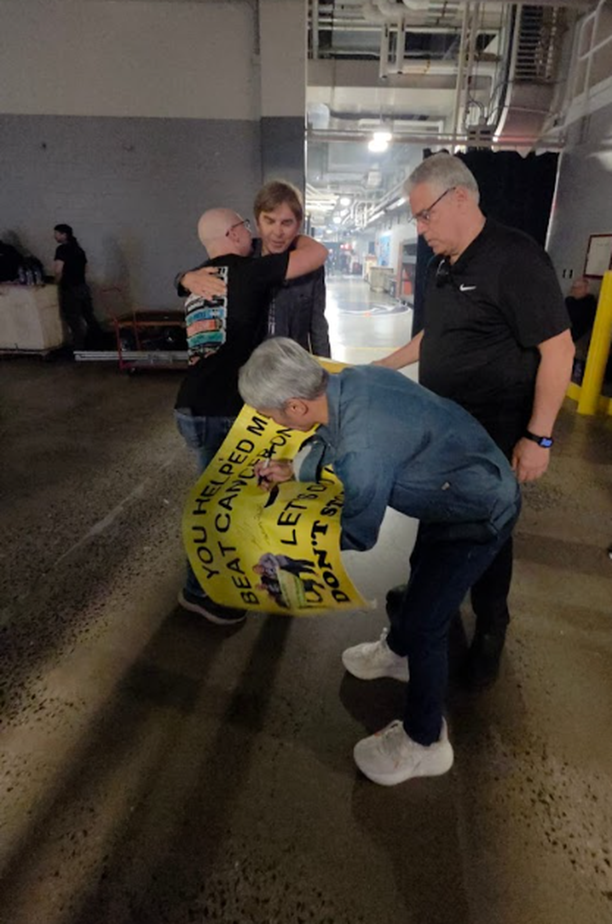 CJ Coudriet hugs Journey keyboardist Jonathan Cain while the band’s frontman Arnel Pineda signs CJ’s banner.