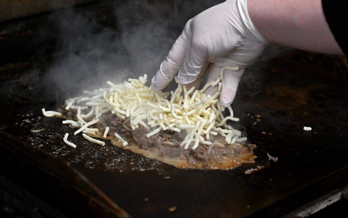 Chad Weller adds the Cooper Sharp American cheese to a cheesesteak at The Phoenix on Wednesday, March 25, 2026. 