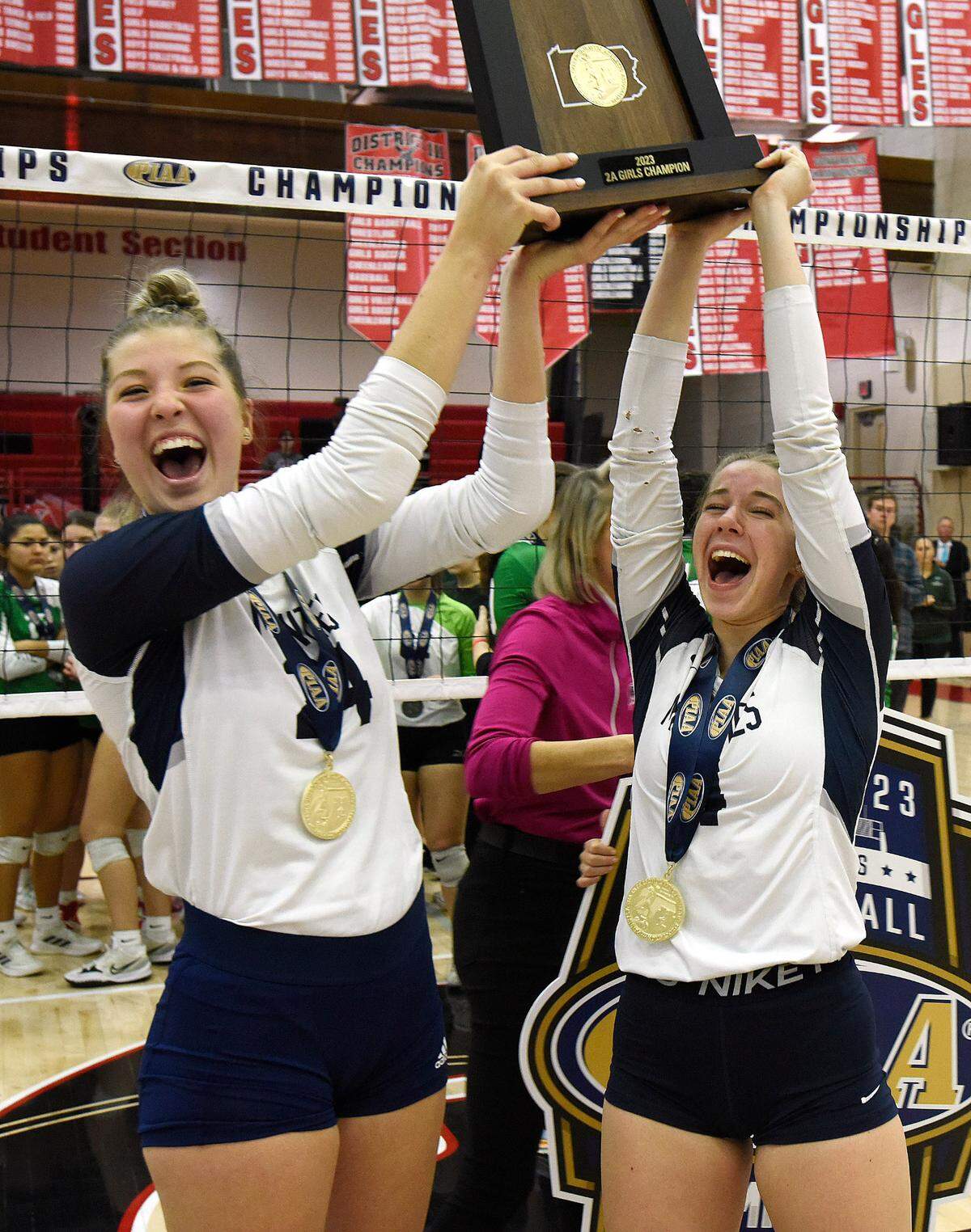 Philipsburg-Osceola’s Reese Hazelton, left, and Sophie Granville hold the PIAA Class 2A state championship trophy Saturday after the Lady Mounties’ girls volleyball team defeated Trinity in four sets in Mechanicsburg at Cumberland Valley.