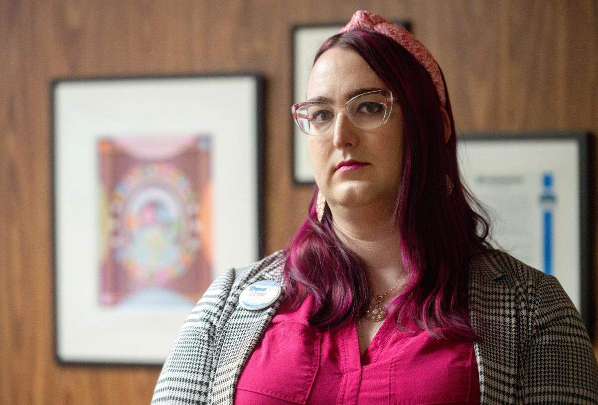 Michel Lee Garrett, a board member for Centre LGBT+, poses for a photos in the lobby of the Centre LGBT+ center on Thursday, Feb. 20, 2025. Art works supporting transgender people and proclamations from the borough hang on the wall behind her.