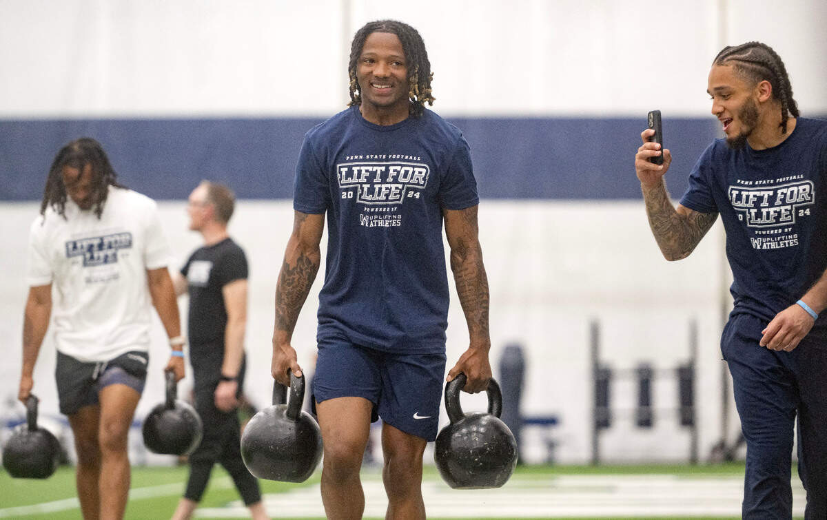 Penn State cornerback Audavion Collins laughs as Cam Miller takes a video of him competing in the kettle bell carry during the 21st Annual Lift for Life to benefit Uplifting Athletes on Thursday, June 13, 2024 in Holuba Hall.