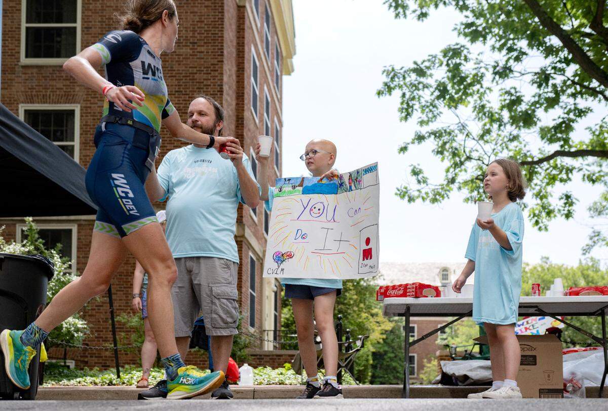 Claire Eichfield holds a sign cheering on runners as she and her family volunteer to hand out drinks to the athletes during the Ironman 70.3 Pennsylvania Happy Valley on Sunday, June 30, 2024.