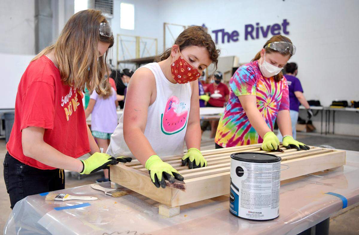 Lexi Whitehill, 11, Kaitlyn Gutierrez, 11, and Lydia Lenz, 13, work together to sand the bench they are making at “GLOW” camp at the Discovery Space on Thursday, Aug. 12, 2021.  The bench will be placed out in the community for everyone to enjoy.  