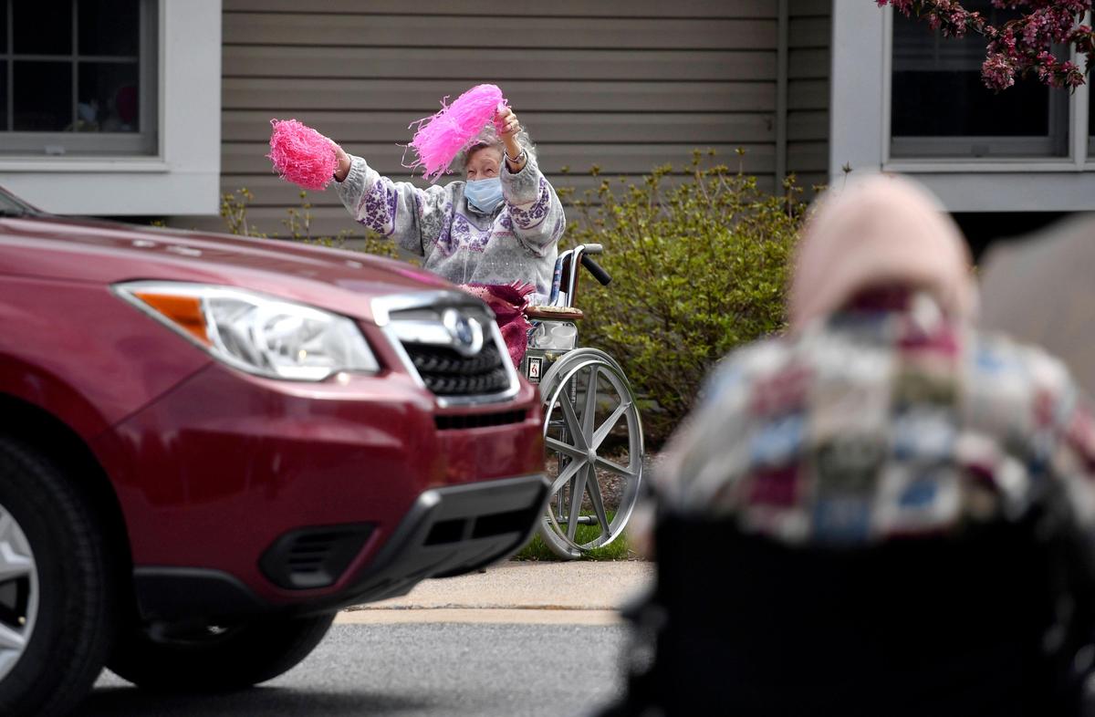Miriam, a resident at Elmcroft State College, waves her pompoms as families drive by in their decorated cars for a Mother’s Day Parade on Sunday