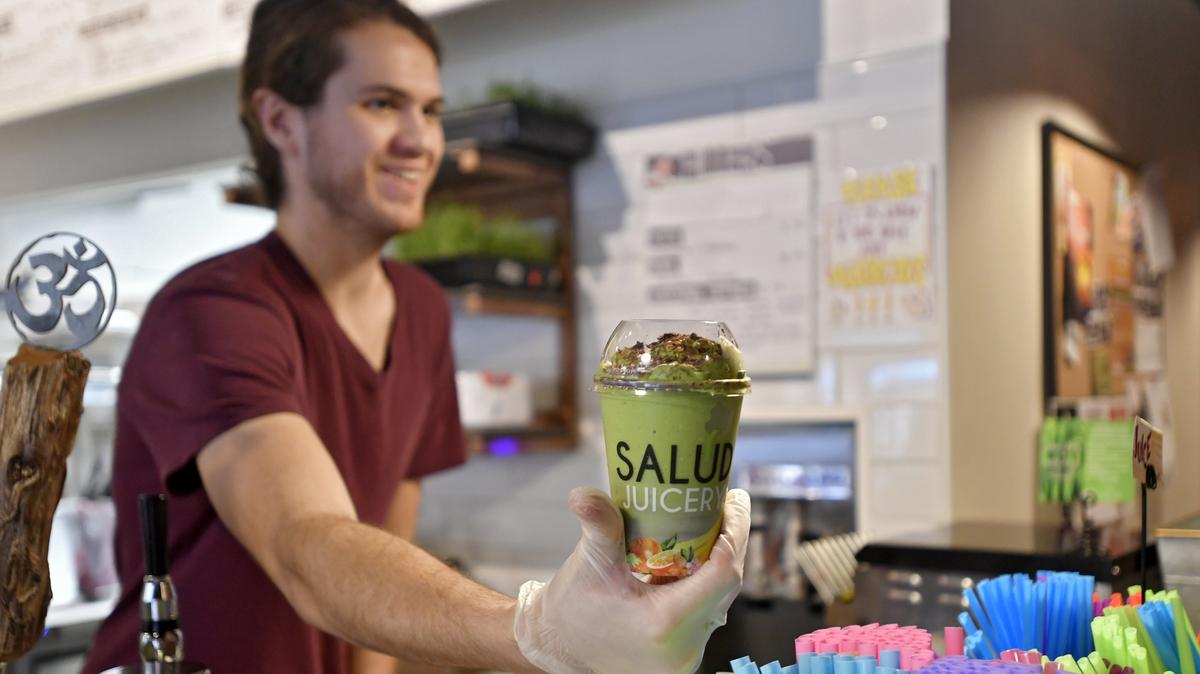 Manager of Salud Juicery Nick Bizousky hands a Green Anna Smoothie to a customer at the State College location on Fraser Street on Monday, July 30, 2018.