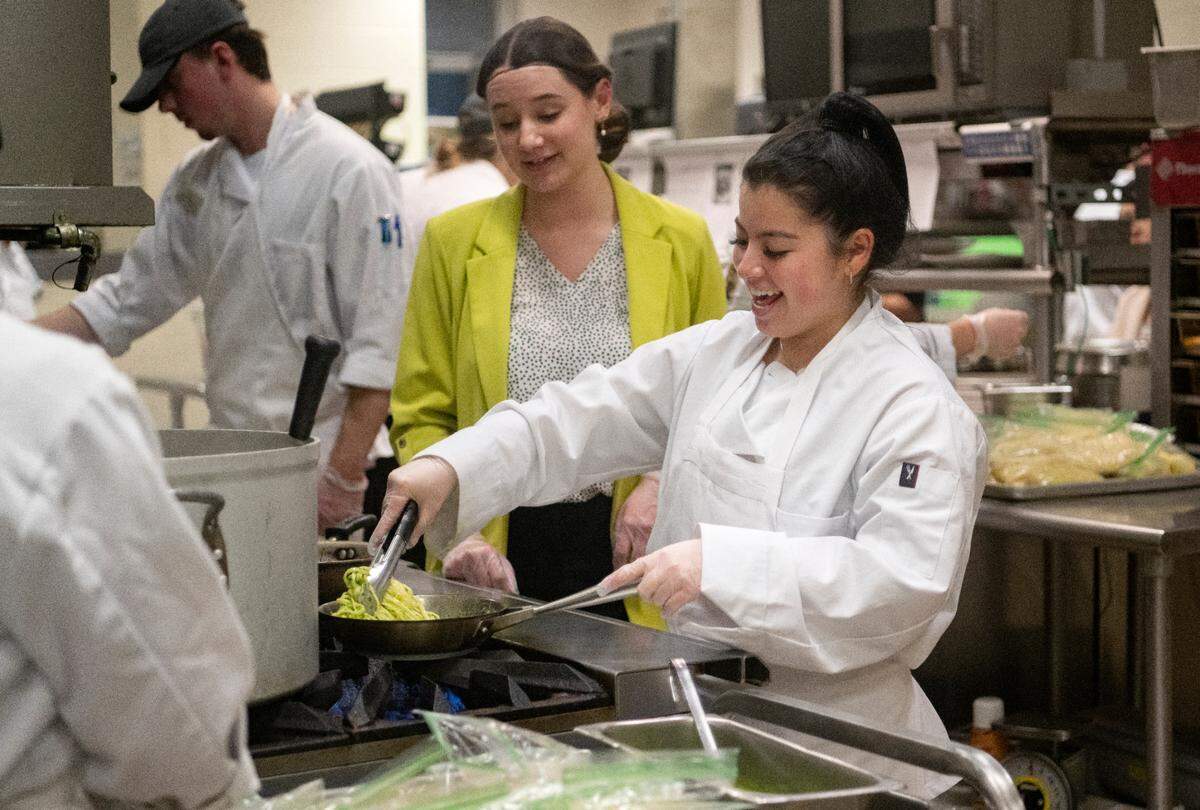 Jessica D’Amico laughs with expo manager Molly Davis as she makes a dish for the Amalfi Dream themed dinner at Cafe Laura on Wednesday, March 1, 2023. Both are Penn State students in the HM430 class.