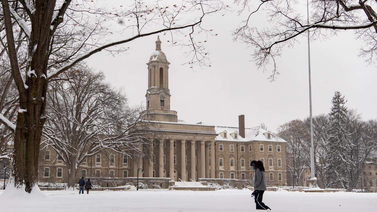 People walk in front of Old Main on the Penn State campus in the snow on Monday, Feb. 1, 2021.