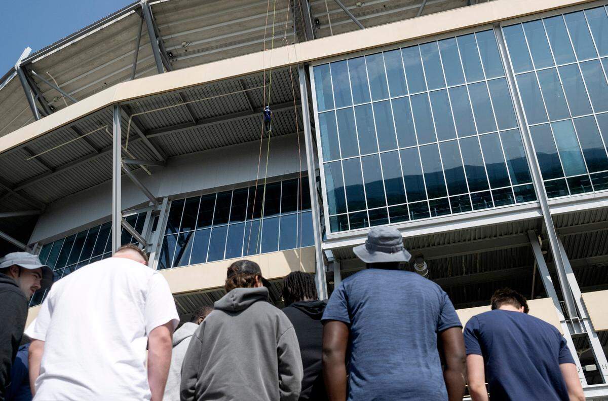 A group of Penn State football players watch as community members rappel from Beaver Stadium for the Centre County United Way Over the Edge fundraiser on Friday, May 19, 2023.