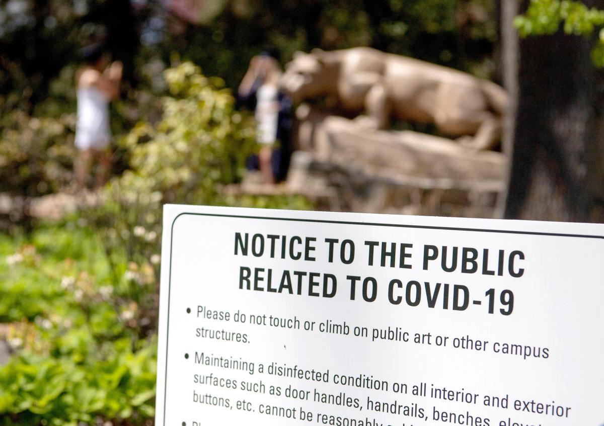 Signs about social distancing and notifying individuals to not touch or climb on campus structures are by the Nittany Lion Shrine Thursday as graduates take photos.