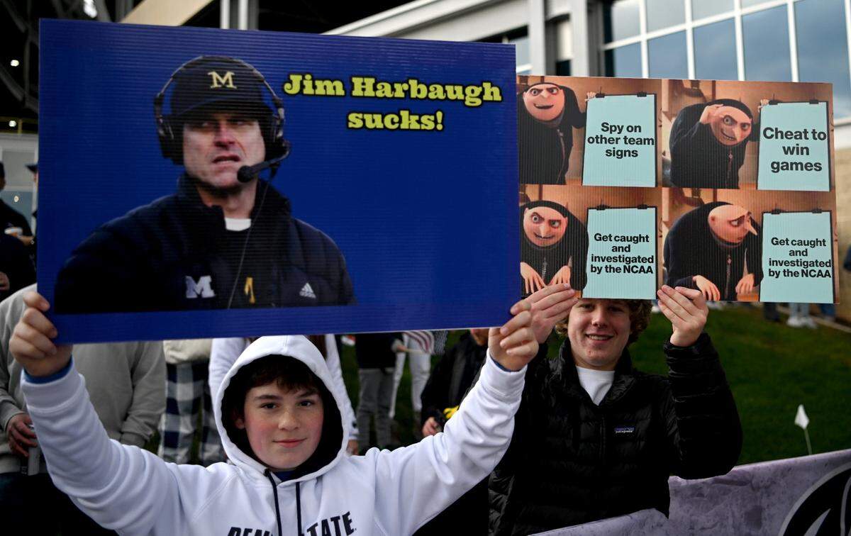Penn State fans hold up signs about Michigan and Jim Harbaugh as they wait for the Penn State team to arrive at Beaver Stadium for the game on Saturday, Nov. 11, 2023.