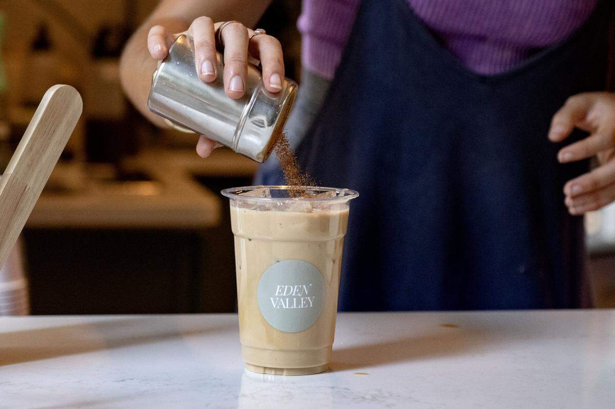 Zoe Duffus sprinkles cinnamon on a Honey Bee signature latte at Eden Valley Coffee Company on Wednesday, July 30, 2025.  