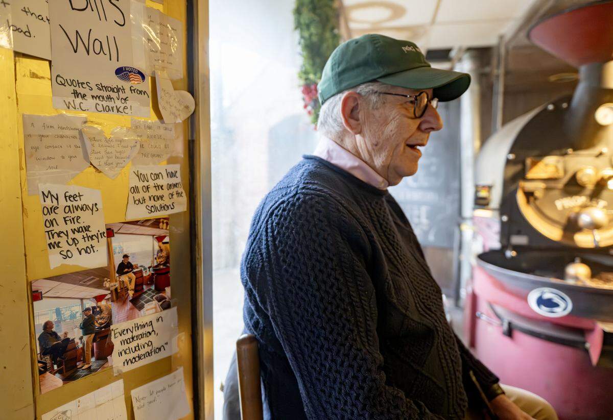 Bill Clarke sits on a stool next to the front door and a wall of things he has said at The Cheese Shoppe on Wednesday, March 4, 2026. 