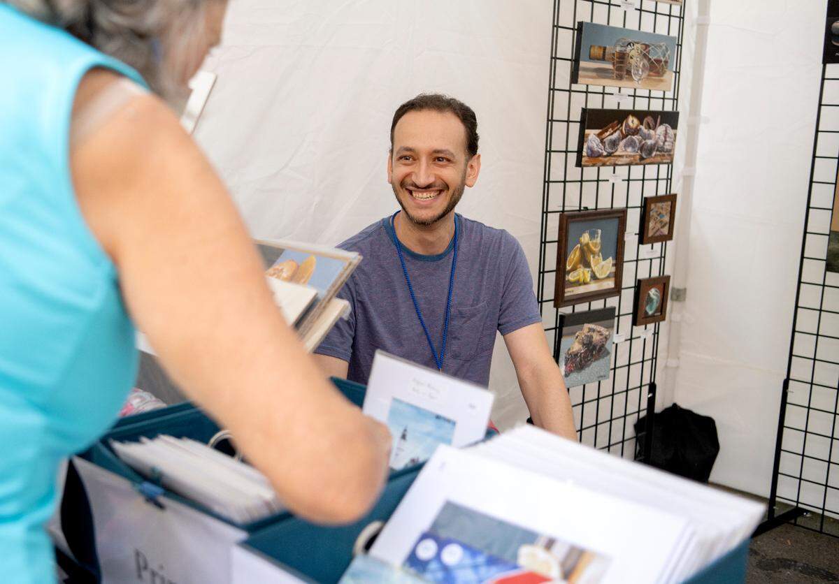 Alexander Ramos laughs with customers as they talk about his paintings at the Central Pennsylvania Festival of the Arts on Thursday, July 14, 2022.