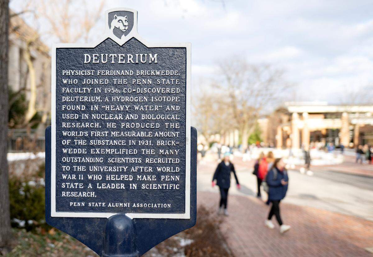 Students walk by the Penn State Alumni Association historical marker for deuterium, a hydrogen isotope co-discovered by a Penn State faculty member in 1956.