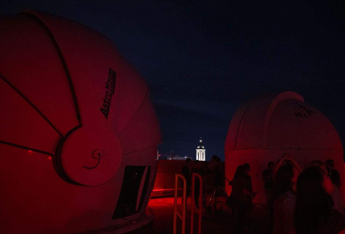 The bell tower of Old Main is illuminated as visitors look through different telescopes on the roof of the Davey Lab as part of AstroFest on Wednesday, July 9, 2025.