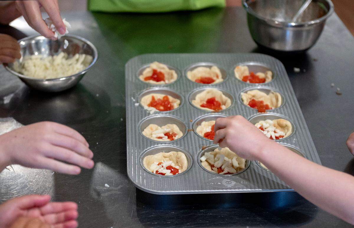 Campers work together to spread the cheese on their deep dish pizza cups during Taste Buds Kitchen summer camp on Tuesday, July 1, 2025.