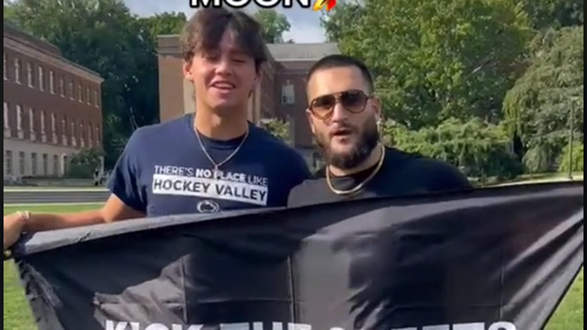 TikTok creator and Penn State Student Brad Kraut stands with a flag in front of a “kick the sheets” flag in a video from Sept. 15, 2022.