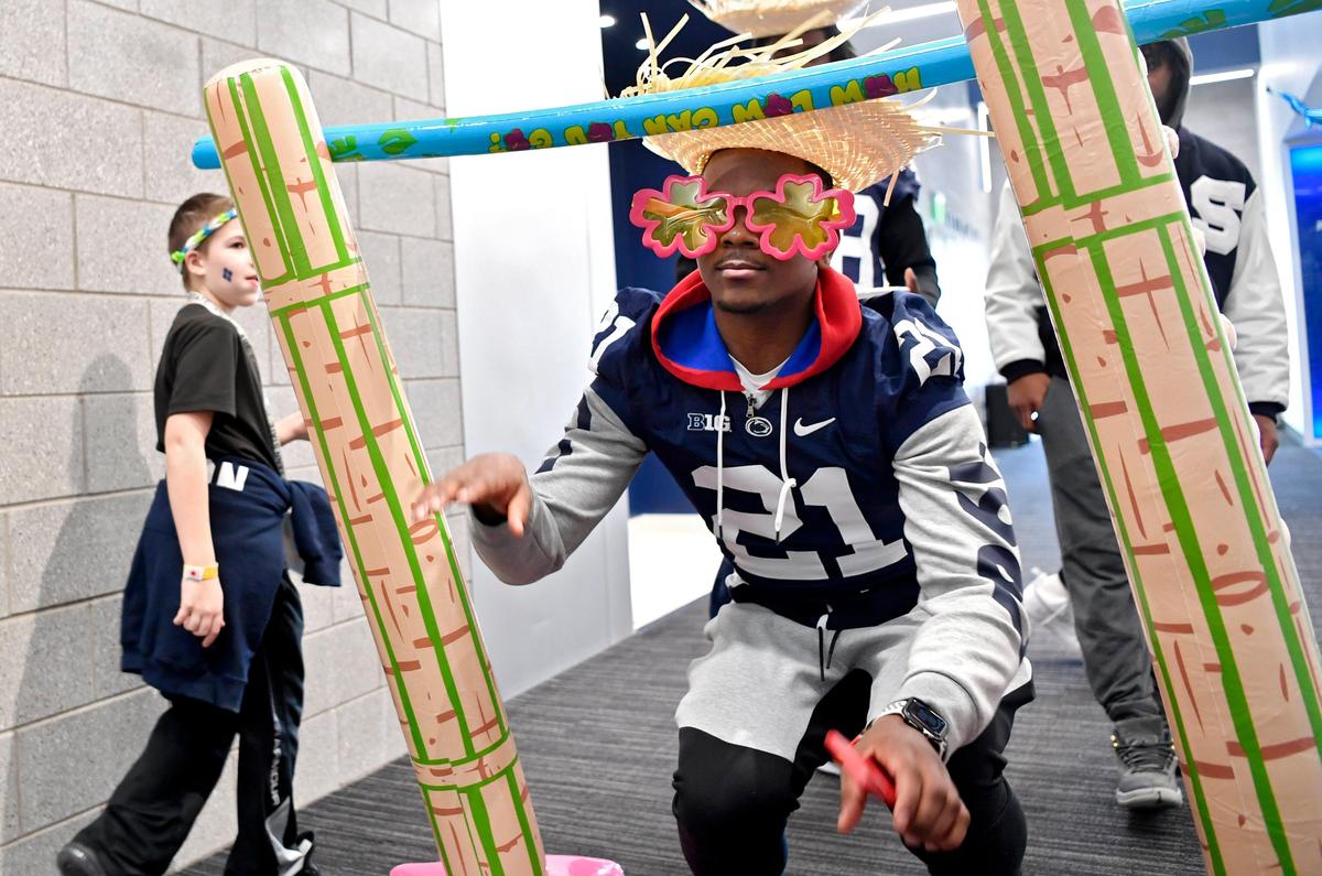 Sporting a straw hat and large flower sunglasses Penn State running back Noah Cain does the limbo with Four Diamonds families in the Lasch Building on Saturday, Feb. 22, 2020.