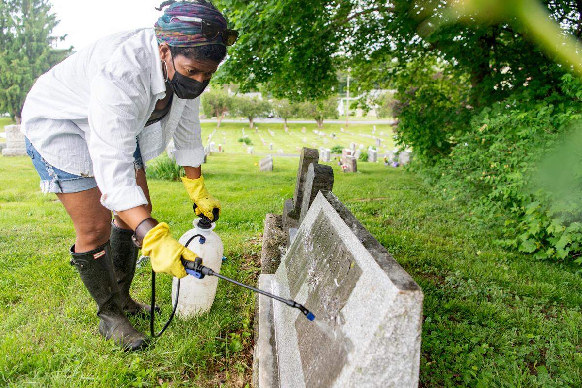 Renea Nichols cleans grave markers at Union Cemetery in Bellefonte on Thursday.