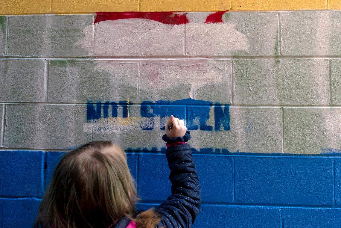 Clara Rochette, 11, helps to paint over the vandalism on the pride wall outside of Jake’s Cards and Games in Bellefonte on Saturday. Under her mask, Clara painted a rainbow flag on her cheek.