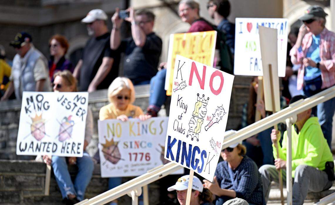 Protesters hold signs on the steps of Old Main as they listen to speakers at the No Kings anti-Trump rally on Saturday, Oct. 18, 2025. 