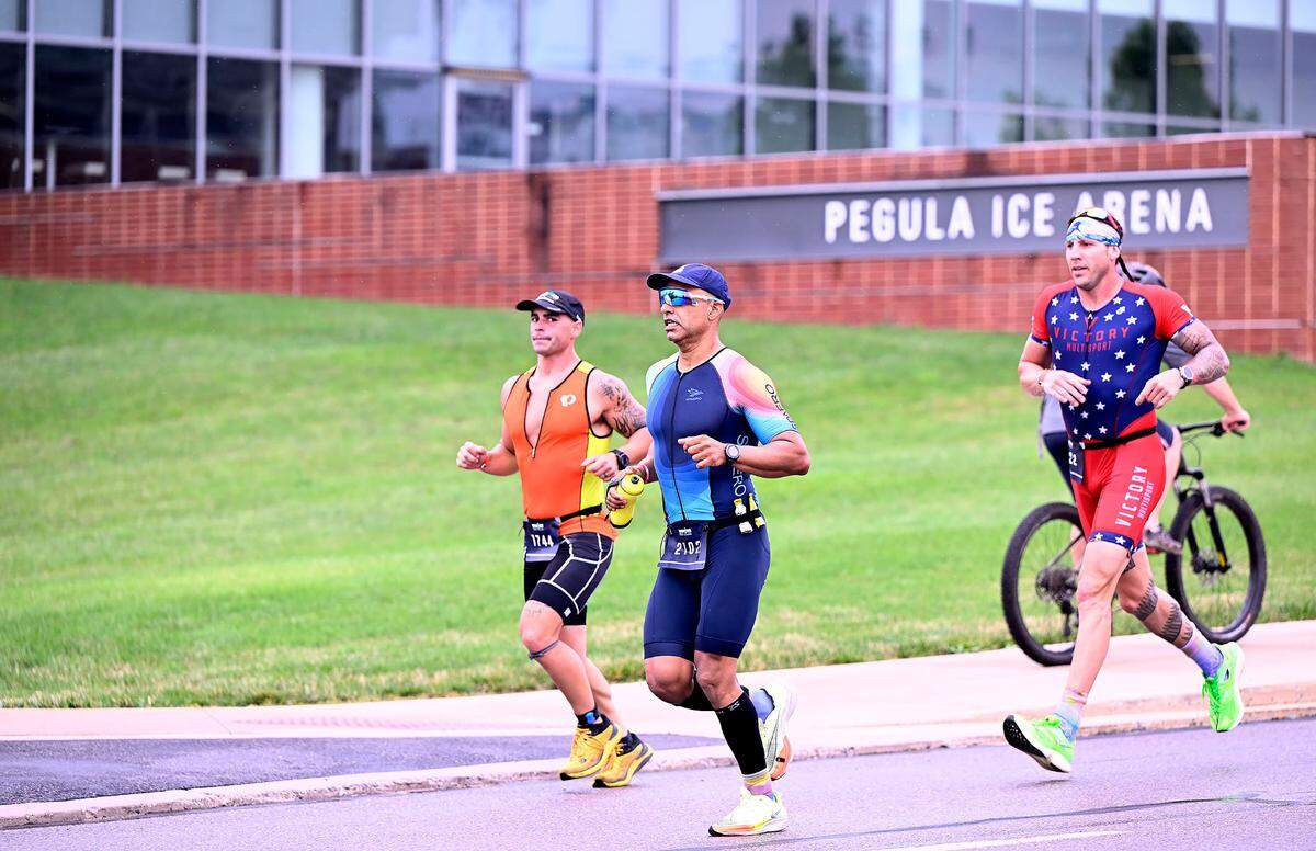 Participants in the Ironman 70.3 Pennsylvania Happy Valley triathlon run past Pegula Ice Arena on the University Park campus Sunday.