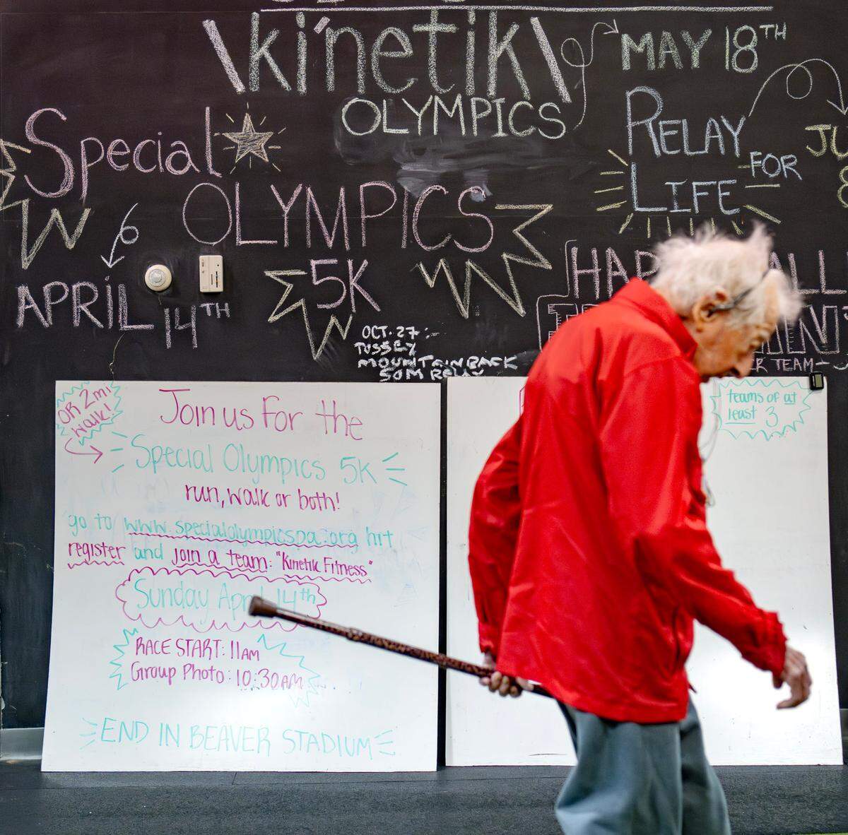George Etzweiler walks past a sign promoting the Ki’netik Fitness team participating in the Special Olympics run on Friday, April 5, 2024. George, who is 104, is training to do the 2 mile walk.