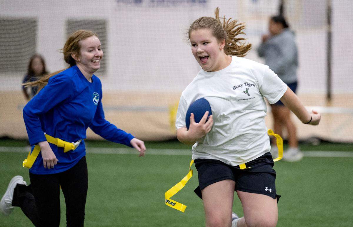 Brooklyn Mergenthaler laughs as she cuts down the field with the ball from coach Dulcia Wigfield during girls flag football practice at Nittany Valley Sports Centre on Wednesday, March 26, 2025.