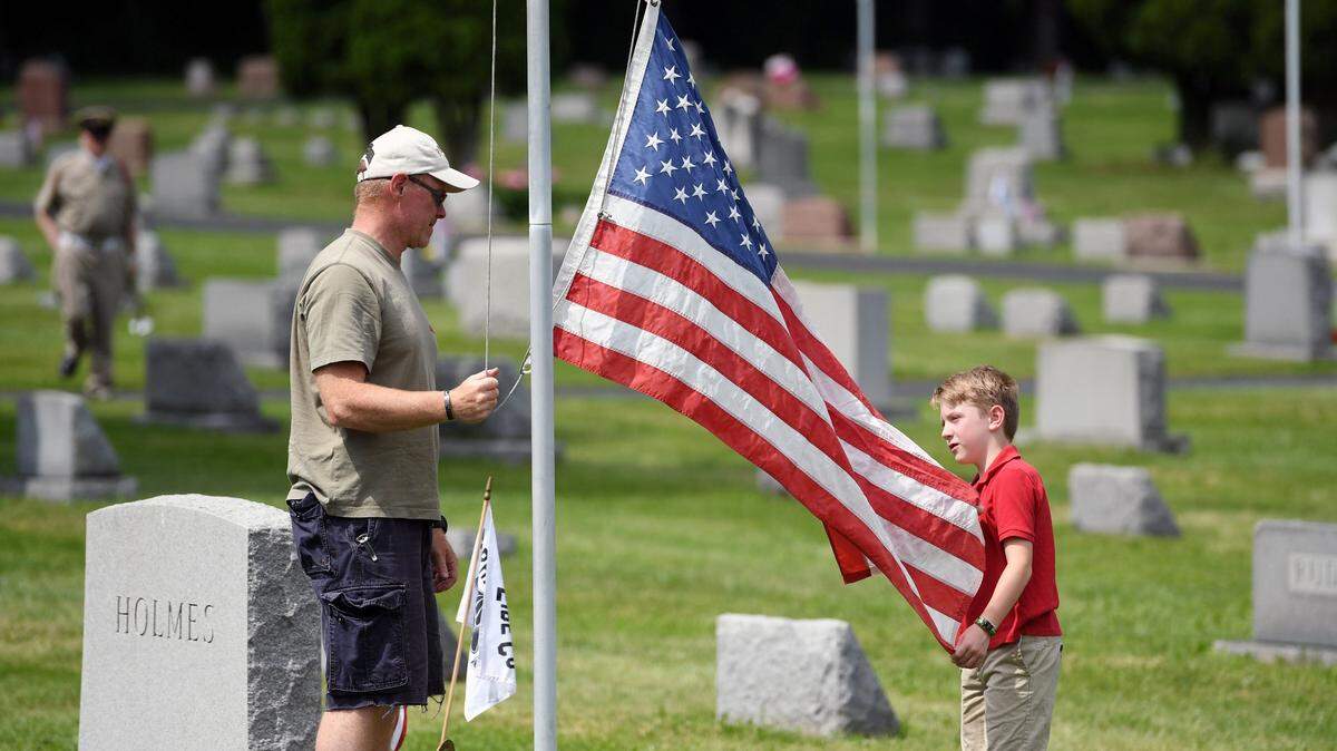 Tom Hammond and his son Lex Hammond, 9, raise a flag during the 30th Pine Hall Cemetery Memorial Day Service Sunday, May 27, 2018 in State College.